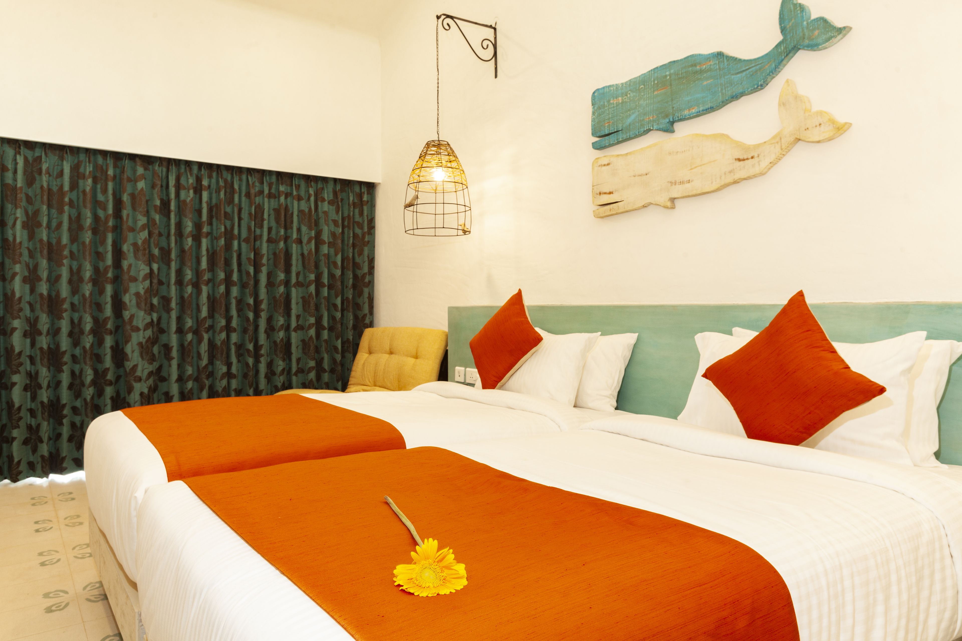 Camera d'albergo con un letto grande, due coperte arancioni, un singolo fiore giallo, un lampadario a parete e una scultura decorativa a forma di balena.