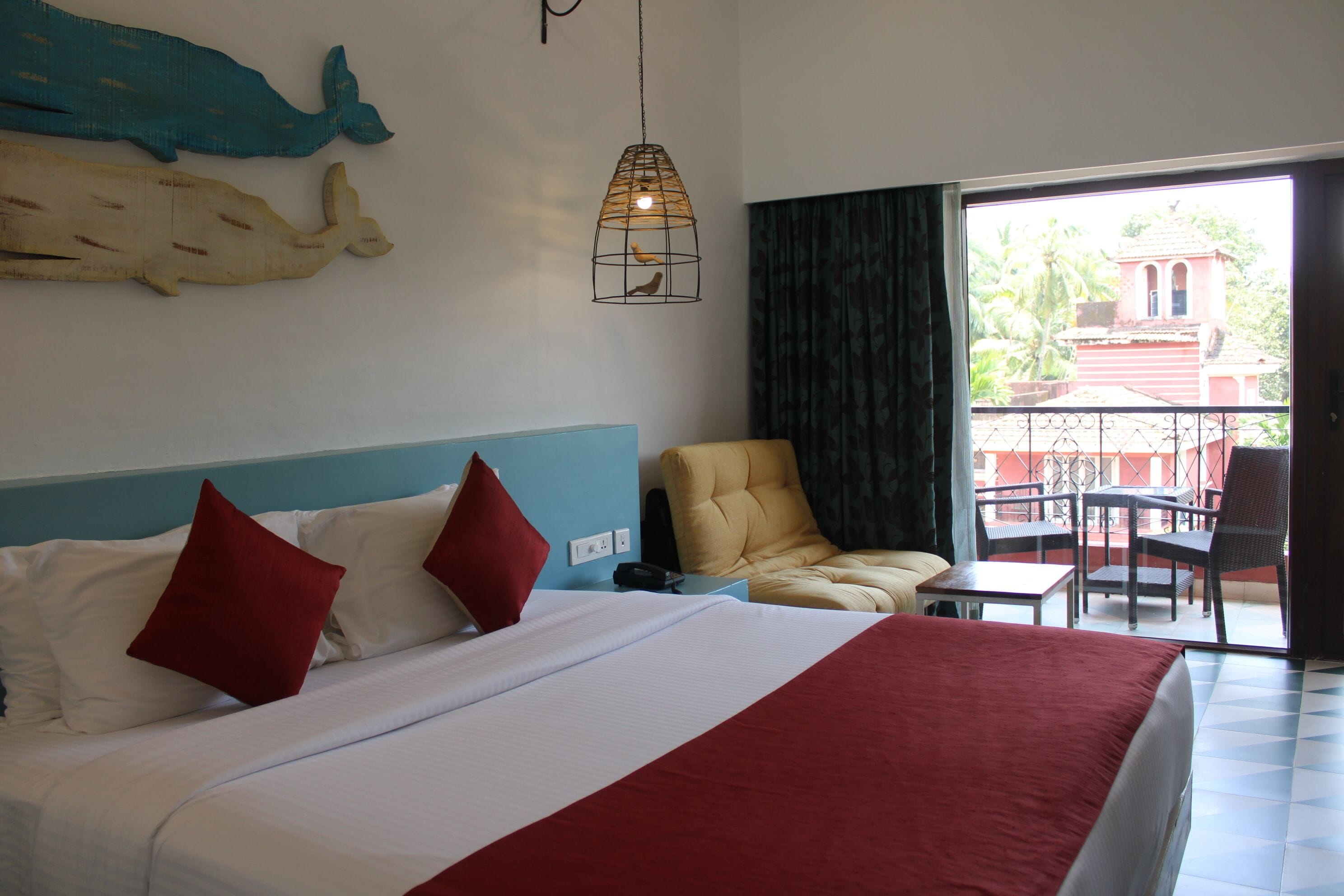 A hotel room with a large bed, a chair, a table, and a balcony with a view of a building.