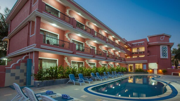 Un hotel de varios pisos con piscina, balcones y mobiliario exterior.