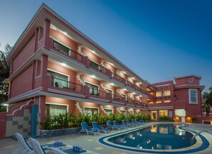 Un hotel de varios pisos con piscina, balcones y mobiliario exterior.