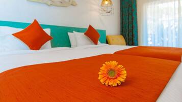 Ein Hotelzimmer mit Bett, orangefarbener Bettwäsche, einem einzelnen orangefarbenen Kissen, einem gelben Sessel, einer Pendelleuchte und einer Wand mit blau-weißem Dekor.