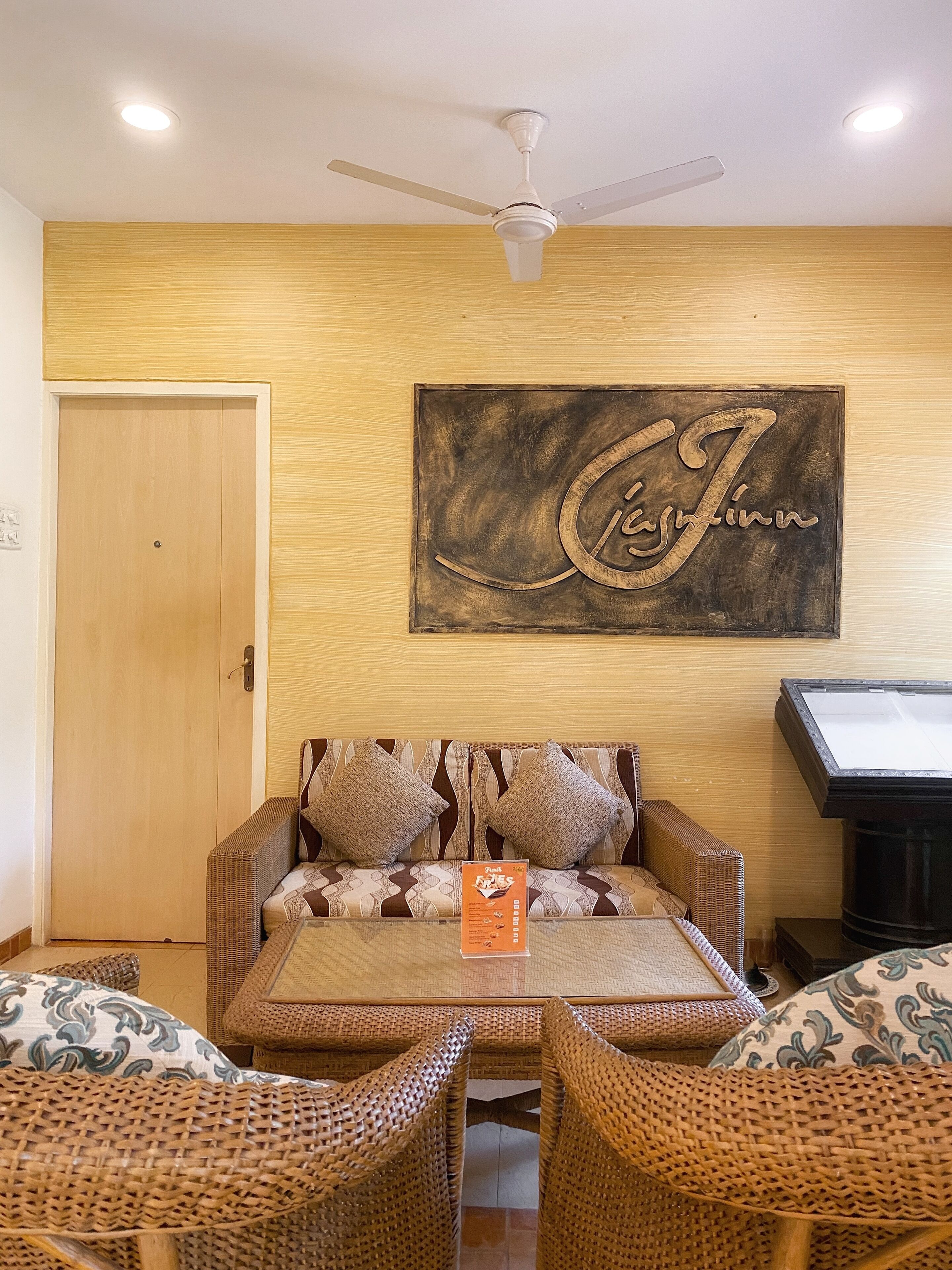 A cozy room with a sofa, two wicker chairs, a ceiling fan, a wooden door, and a wall-mounted artwork.