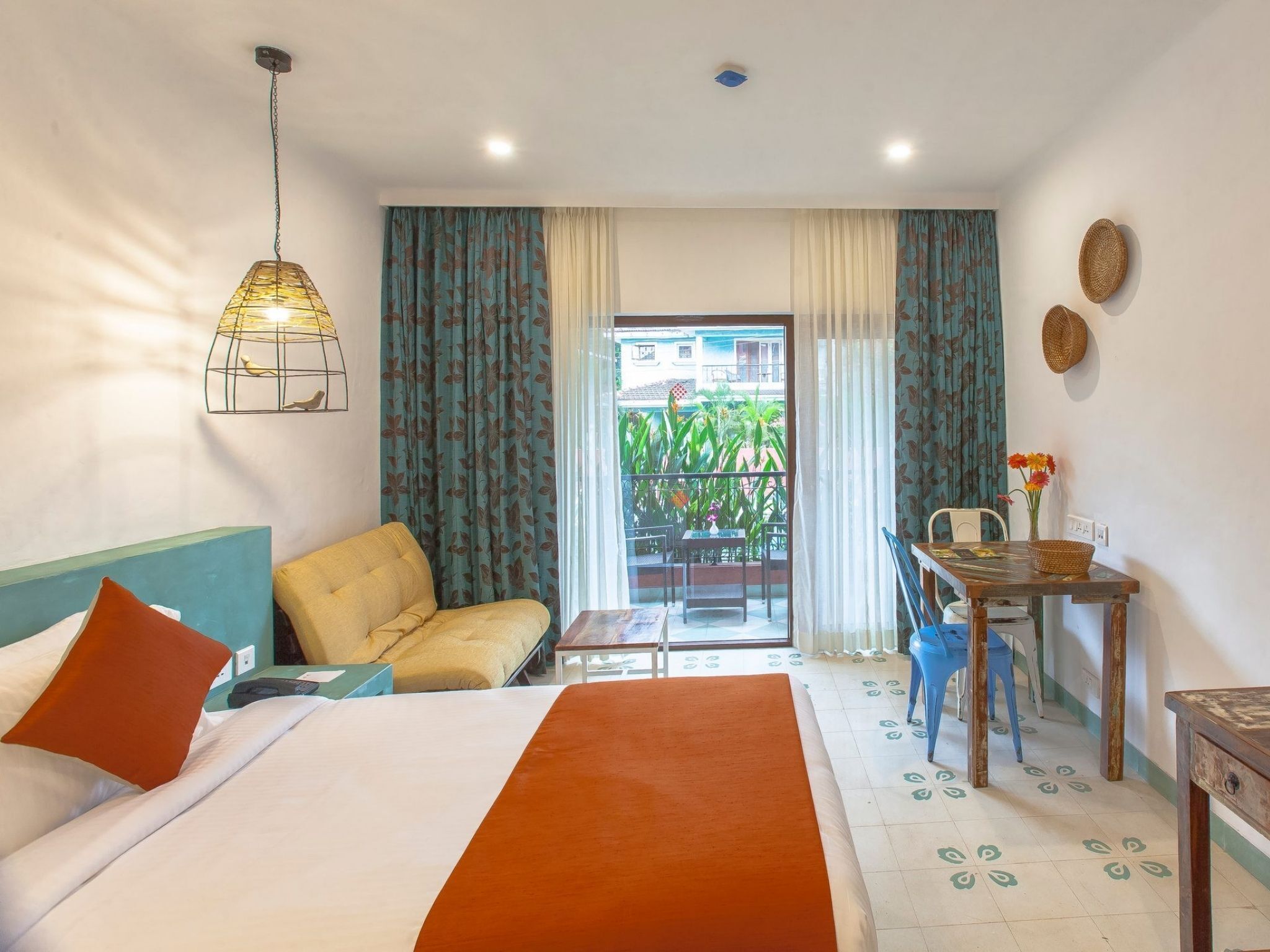 Habitación de hotel con cama, sofá, mesa con un florero y vista al exterior.