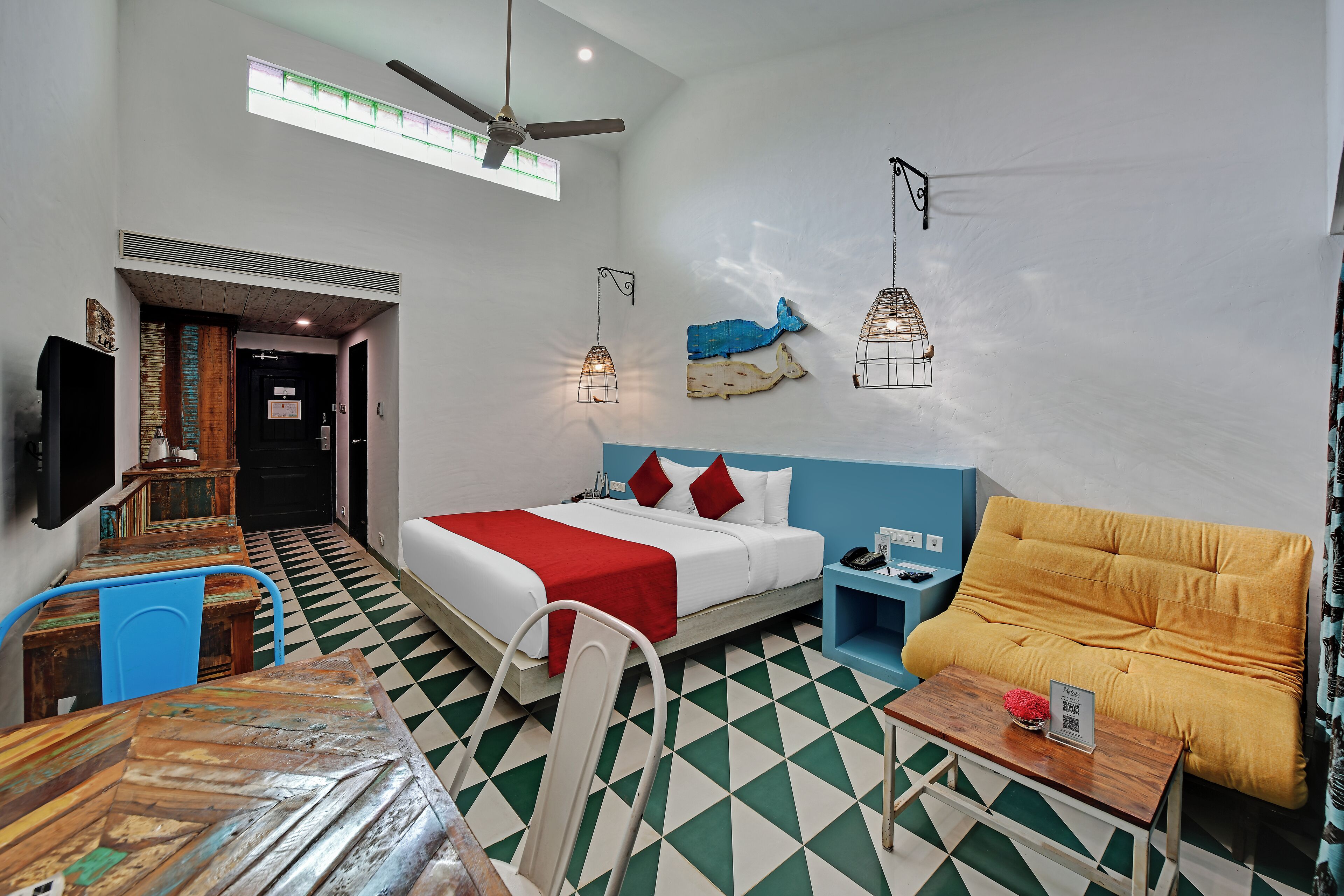 A hotel room with a bed, a sofa, a table, a TV, and a ceiling fan.