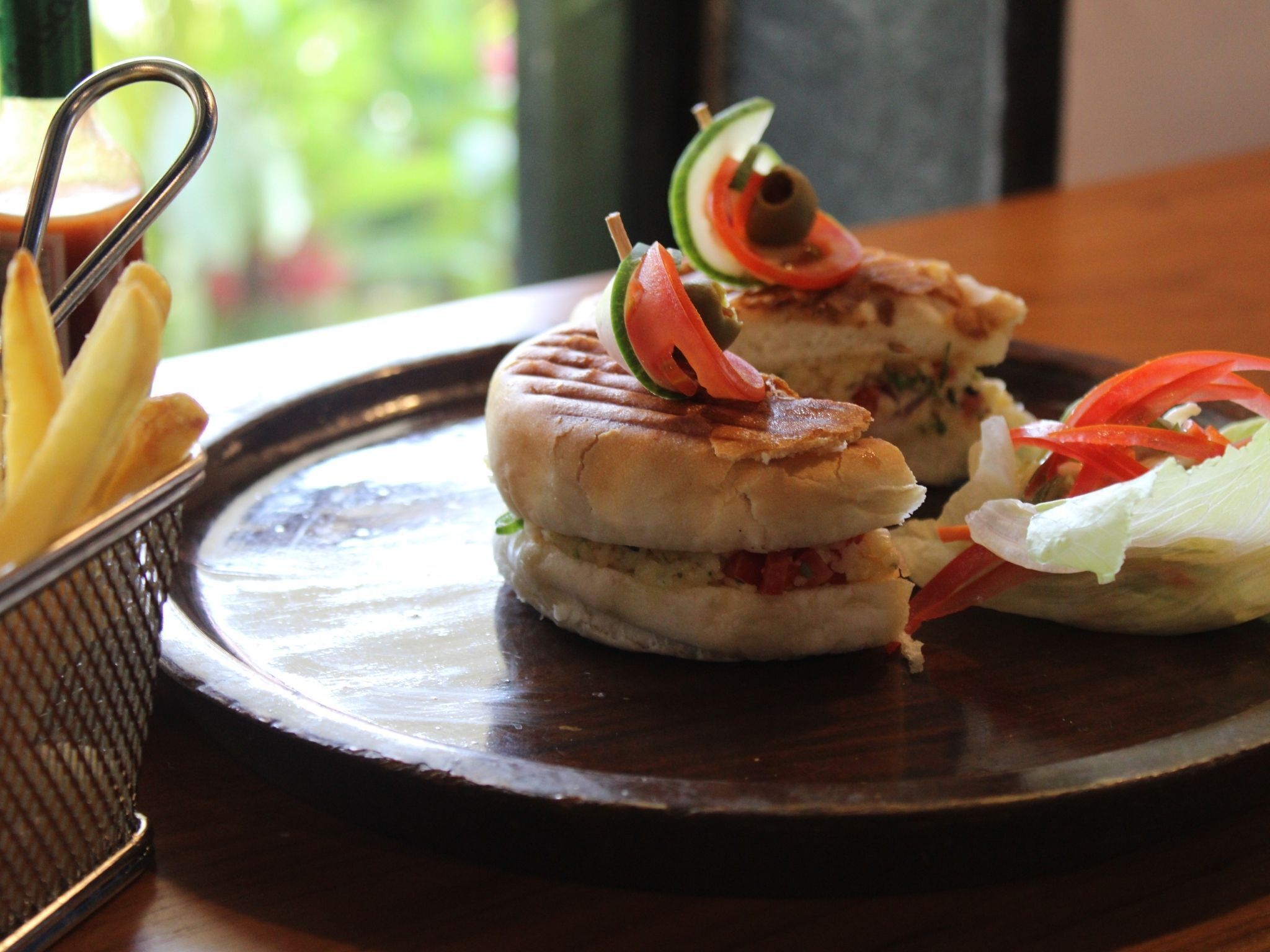 A sandwich with tomato and cucumber on a plate, accompanied by fries and a small salad.