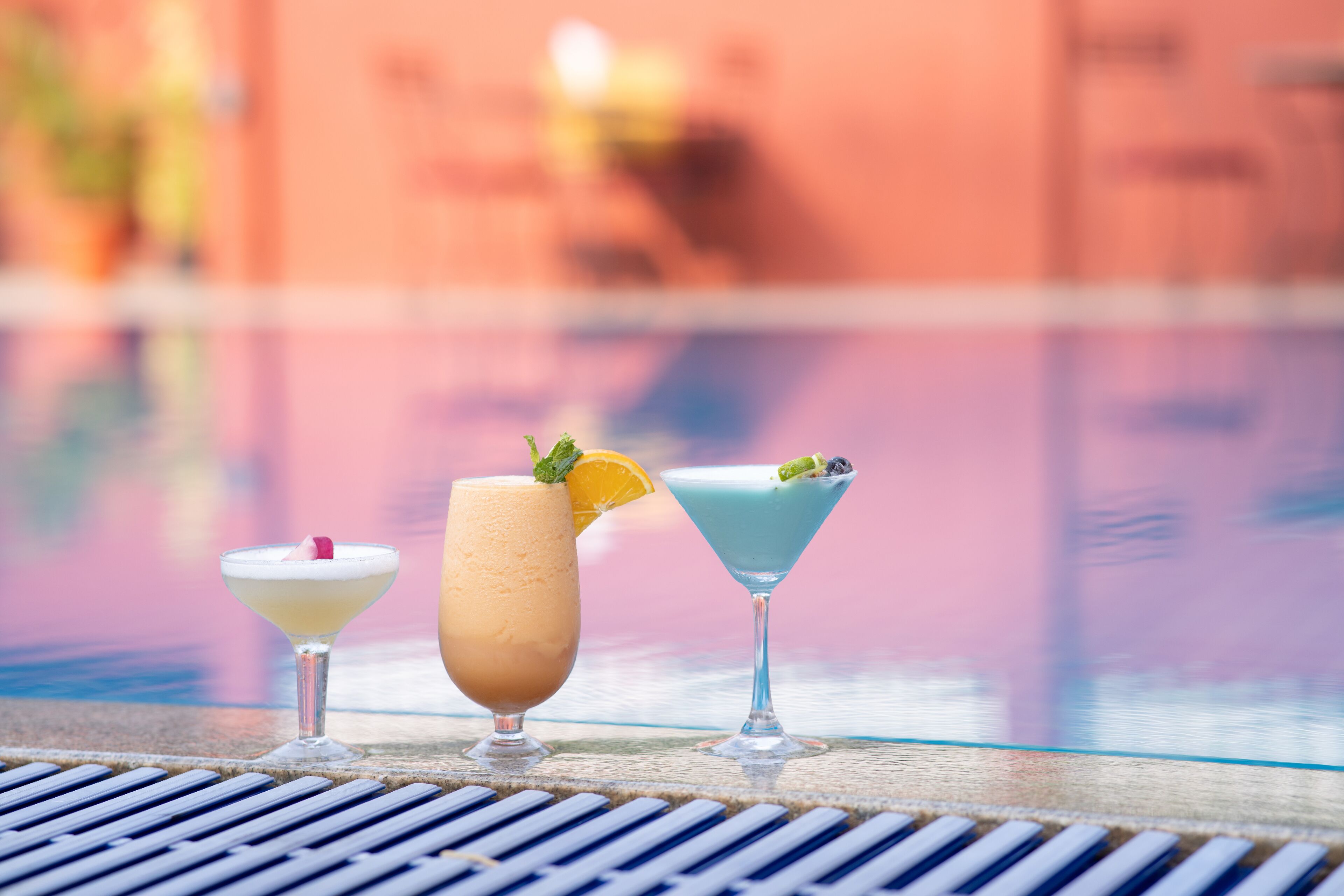 Three cocktails on a table by a poolside.