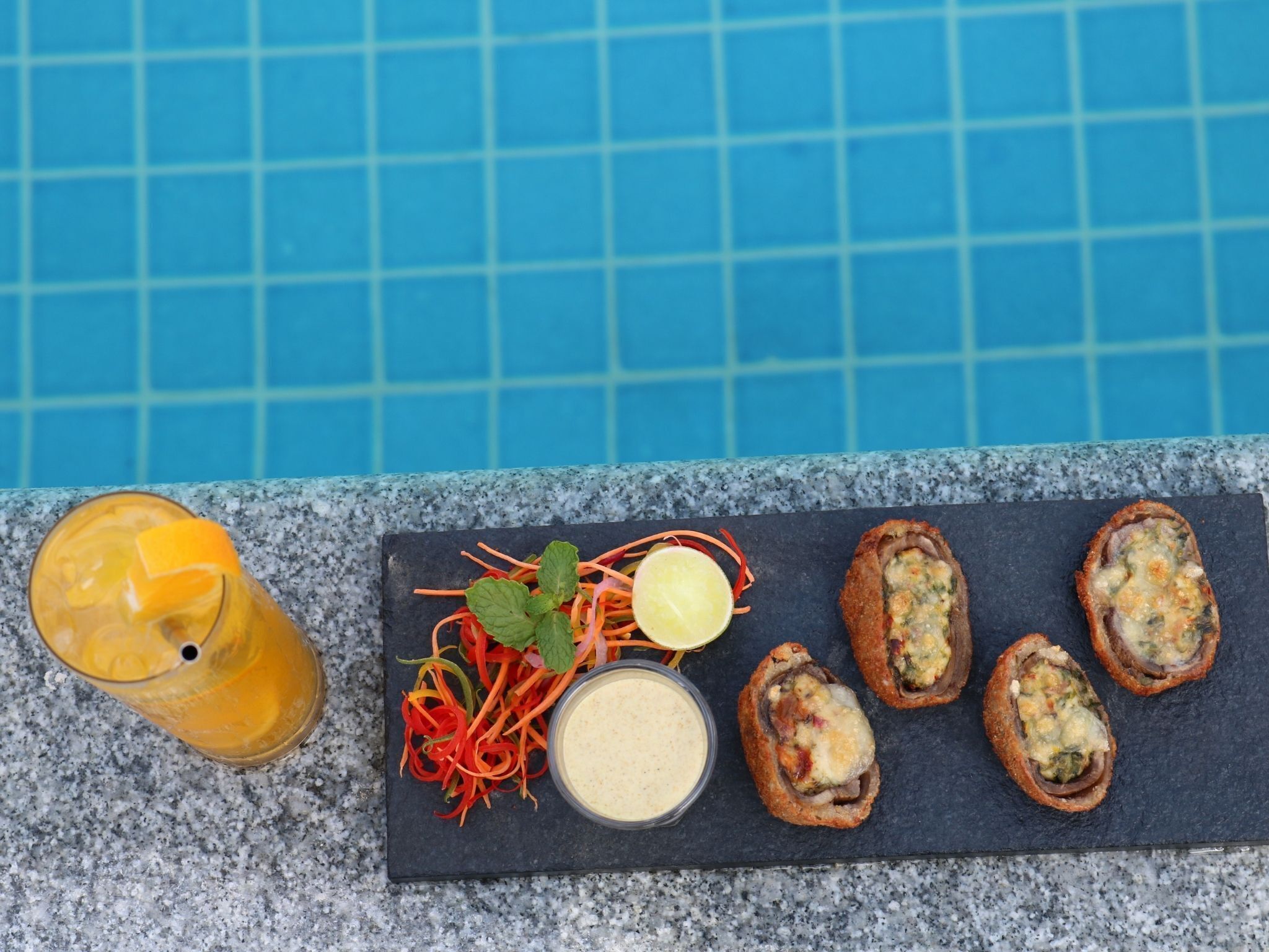 Un repas composé d’un verre de jus d’orange, d’une salade et de quelques plats panés, le tout présenté sur une ardoise.