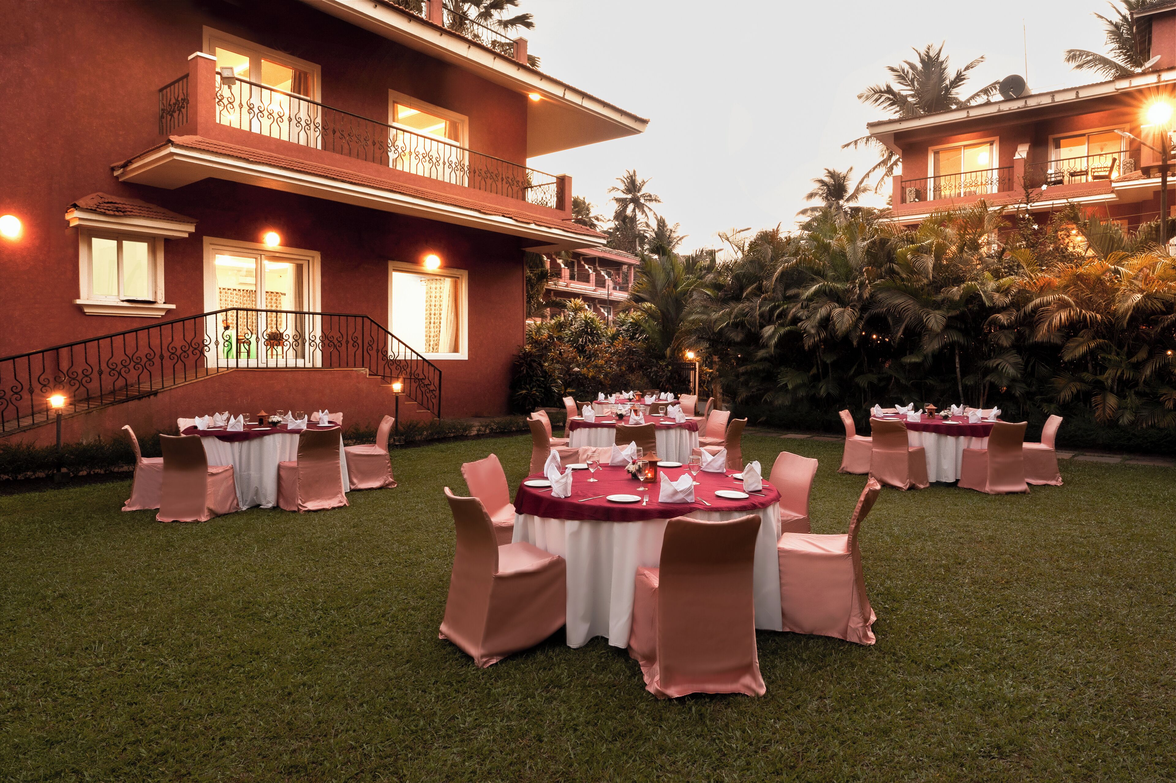 An outdoor dining area with round tables and chairs, set against a building with balconies and a staircase.