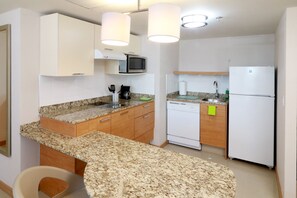 A compact kitchen with granite countertops, a microwave, a dishwasher, and a refrigerator.