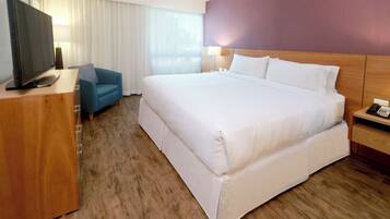 A hotel room with a large bed, a television on a wooden desk, a blue armchair, and a nightstand with a phone.