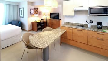 Una habitación de hotel con cama, un escritorio con silla, una kitchenette con microondas y un comedor con mesa y sillas.