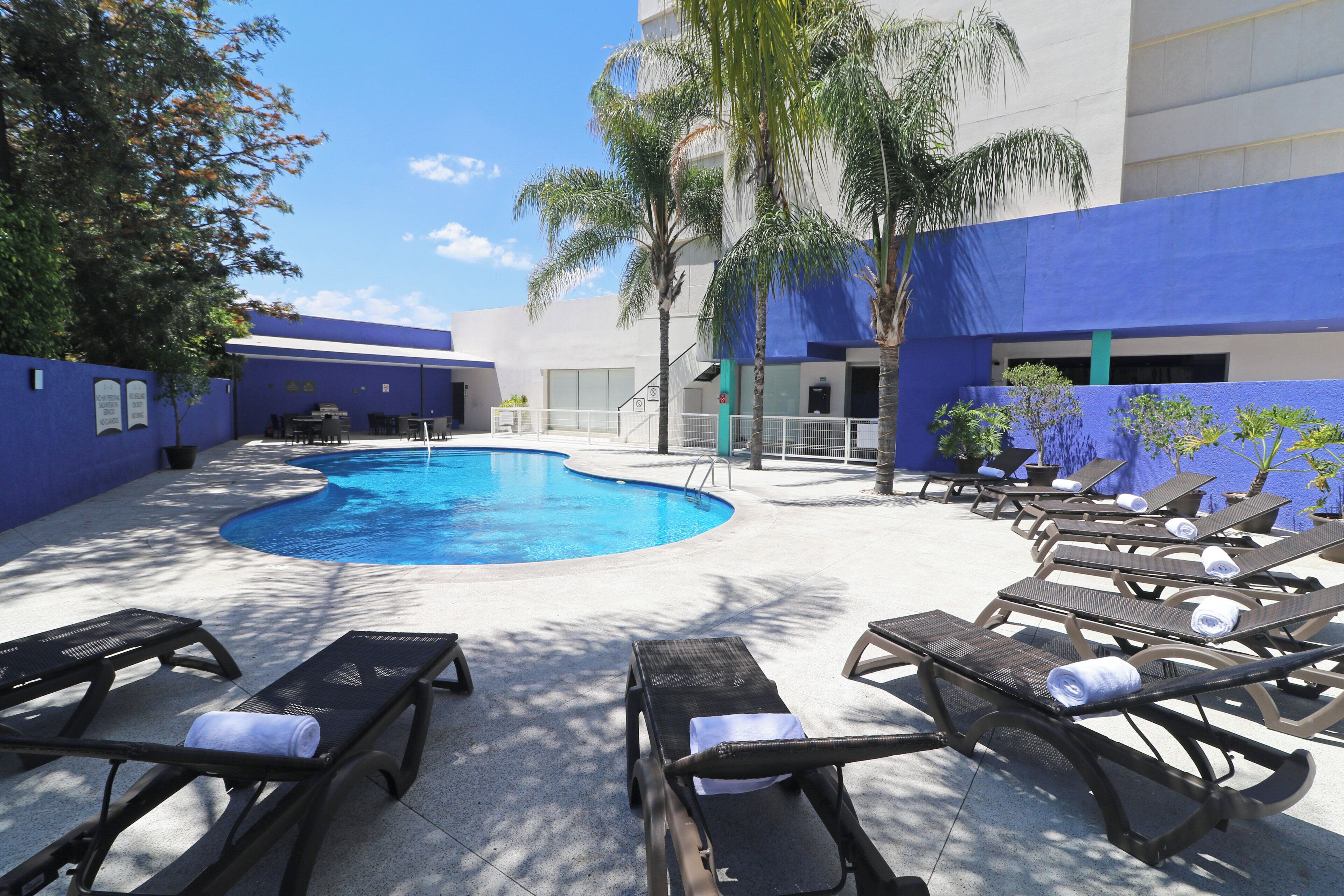 Un área de piscina con sillones de descanso y un edificio azul.
