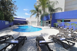Un área de piscina con sillones de descanso y un edificio azul.