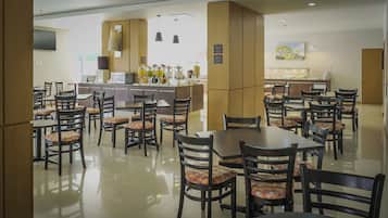 Ein Essbereich eines Hotels mit mehreren Tischen und Stühlen, einer Küche im Hintergrund und einer großen Säule.