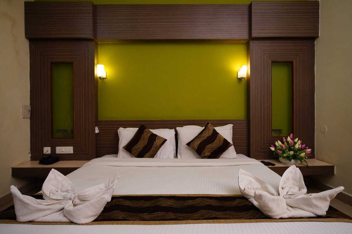 Une chambre d’hôtel avec un grand lit, deux lampes de chevet, un mur d’accent vert et un vase à fleurs sur la table de chevet.