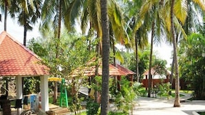 A pathway lined with palm trees and small structures with red roofs, surrounded by well-maintained grass and a clear sky. - Green Coconut Resort (Tirupporur)