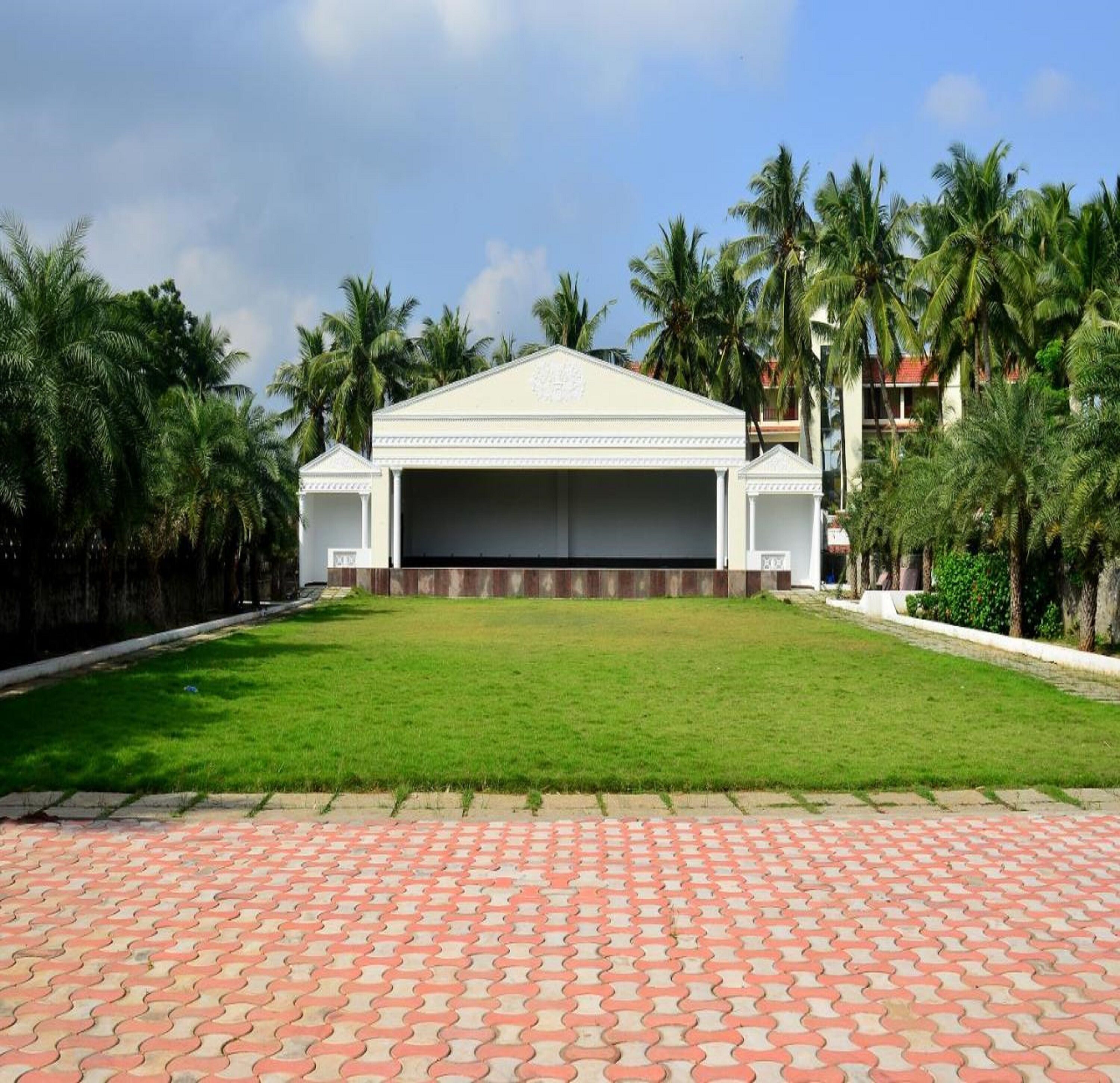 A large, white building with a flat roof and a central entrance, surrounded by a well-maintained lawn and palm trees.