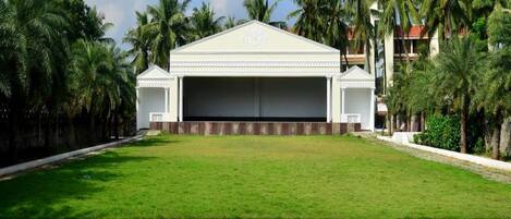 A large, white building with a flat roof and a central entrance, surrounded by a well-maintained lawn and palm trees.