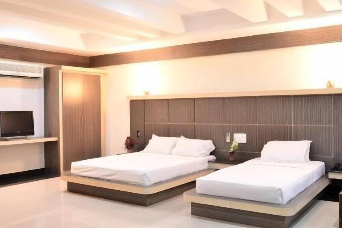 Une chambre d’hôtel moderne avec deux lits, un téléviseur à écran plat et une tête de lit en bois.