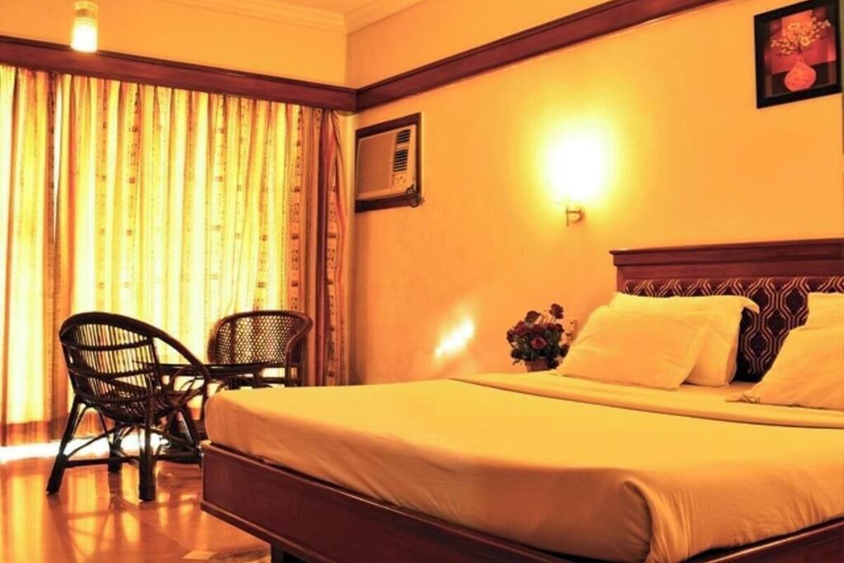 Une chambre d’hôtel comprenant un lit, deux chaises, un climatiseur fixé au mur et un luminaire fixé au mur.