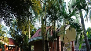 A building with a curved roof, surrounded by lush greenery and palm trees. - Green Coconut Resort (Tirupporur)
