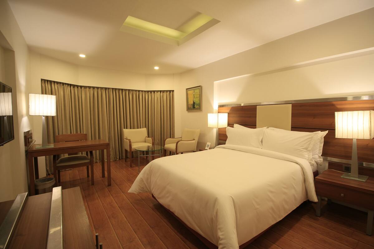 A hotel room with a large bed, a desk with a chair, a small table, and a TV.