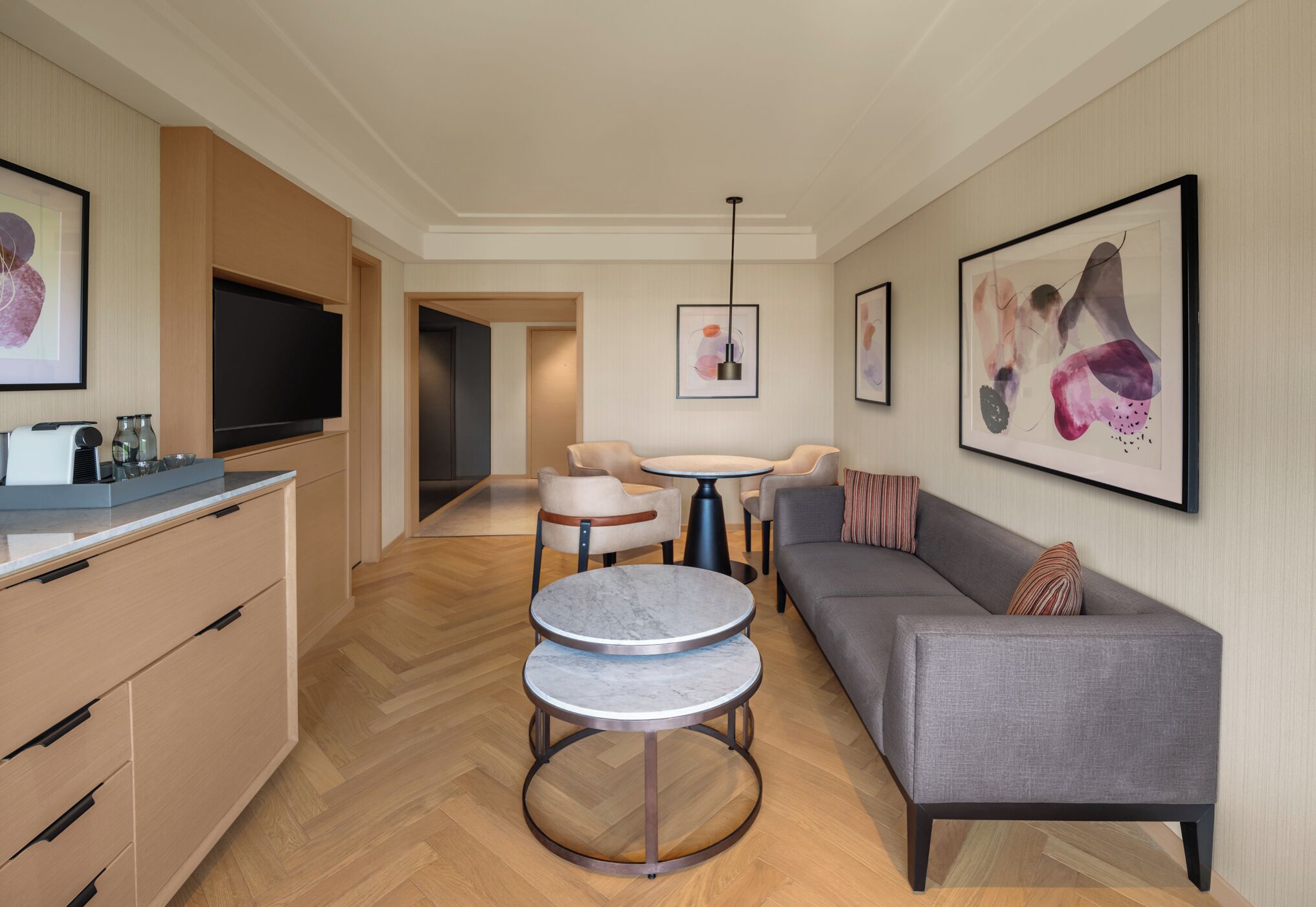 A modern hotel room with a sofa, two round tables, a TV, and artwork on the walls.