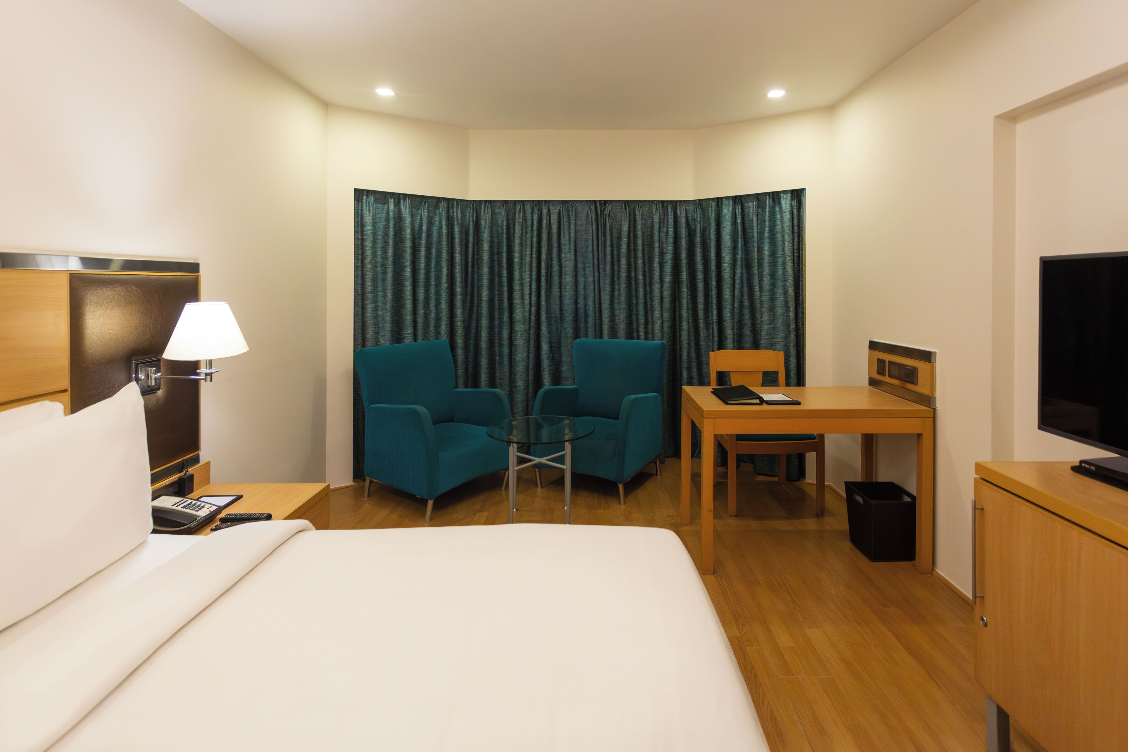 Una habitación de hotel con una cama, un escritorio, dos sillas, un televisor y una lámpara.