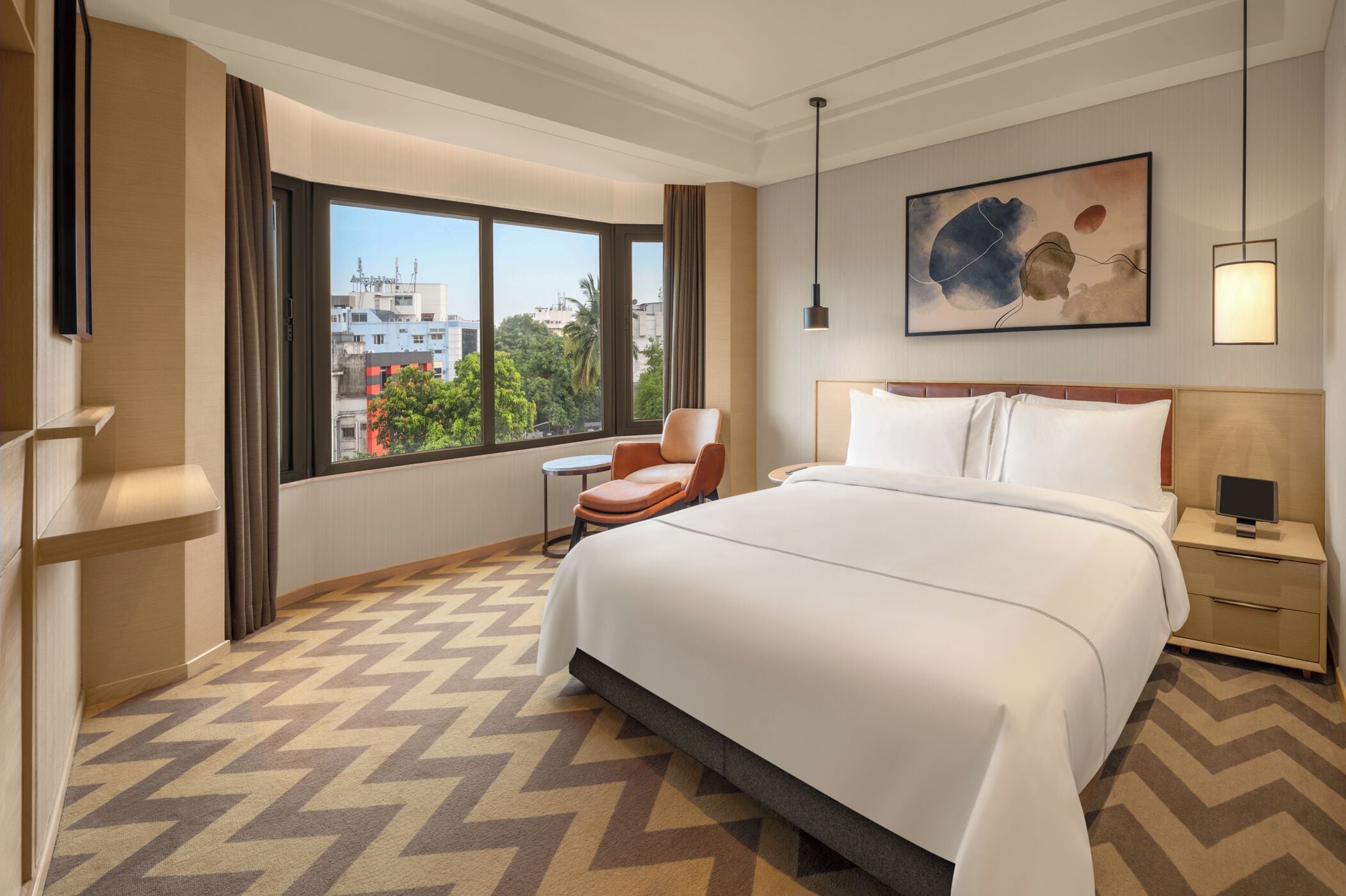 Una camera d'albergo con un letto grande, una sedia, un comodino, una lampada e un quadro appeso al muro.