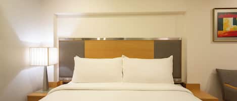 A hotel room with a bed, a nightstand, a lamp, and a chair.