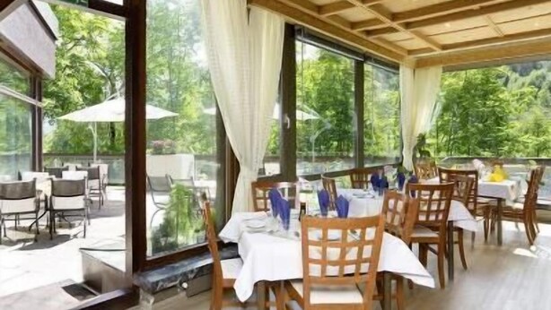 An outdoor dining area with tables and chairs, large windows, and a view of greenery. - Europark Hotel International (Fuessen)