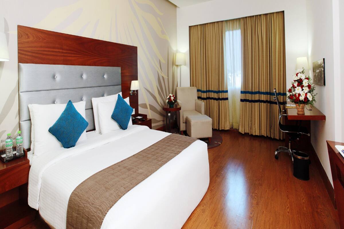 A hotel room with a large bed, a desk, a chair, and a window with curtains.
