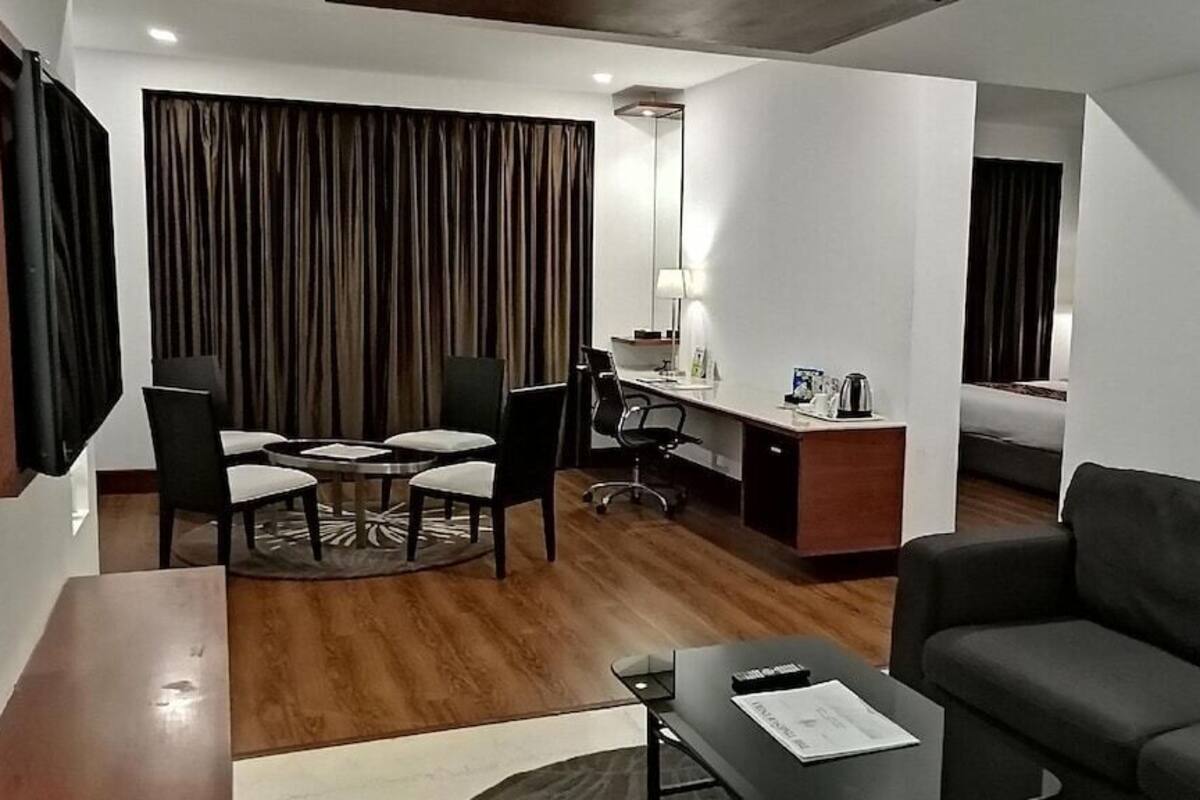 A modern hotel room with a wooden floor, a sofa, a desk with a chair, a TV, and a bed.