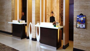 A reception area with two receptionists, a marble wall, and a bulletin board with pamphlets. - Hotel Abu Palace - Chennai (Chennai)