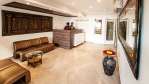 Zona de recepción con mostrador, un sofá, una mesa de centro y un jarrón decorativo con flores.
