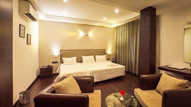 Habitación de hotel con una cama grande, dos mesitas de noche, un sofá, una pequeña mesa con un florero y un espejo en la pared.