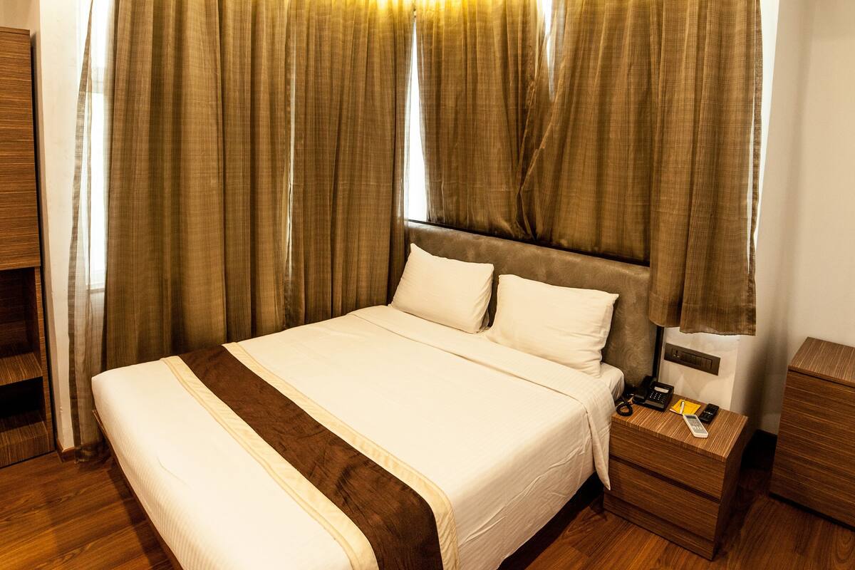 A modern hotel room with a large bed, wooden flooring, and a nightstand with a lamp.