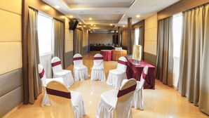 Un salón de conferencias con filas de sillas blancas adornadas con listones rojos, mesas cubiertas con manteles rojos y una mesa larga con camino de mesa blanco y una vela alta.