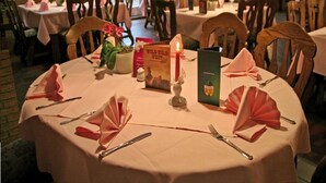 A restaurant with round tables set for dining, featuring a candle centerpiece, menus, and folded napkins. - Hotel Kaiserquelle (Salzgitter)