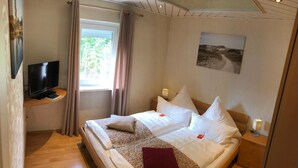 A hotel room with a bed, a TV on a stand, a window with curtains, and a painting on the wall. - Hotel Kaiserquelle (Salzgitter)