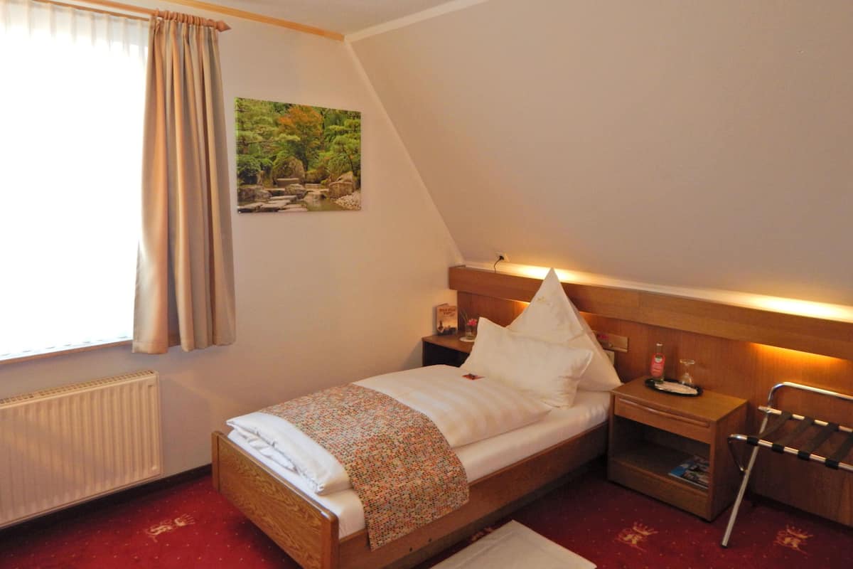 A bedroom with a wooden bed, a nightstand, a chair, a radiator, and a window with curtains.