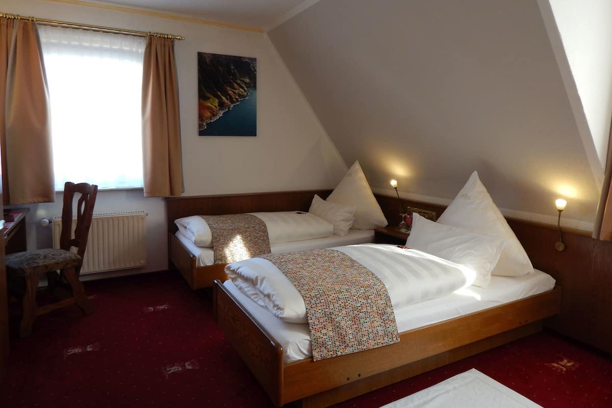 A bedroom with a wooden bed, two pillows, a nightstand, a chair, a radiator, a window with curtains, and a painting on the wall.