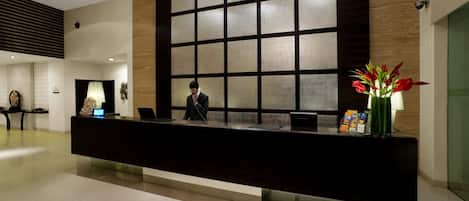 A modern reception desk with a large window, a receptionist, and a vase with flowers.