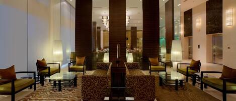 A modern lobby with a central seating area, glass partitions, and a chandelier.