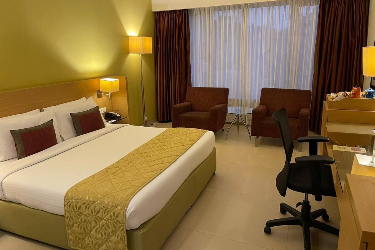 A hotel room with a large bed, two armchairs, a desk, and a lamp.