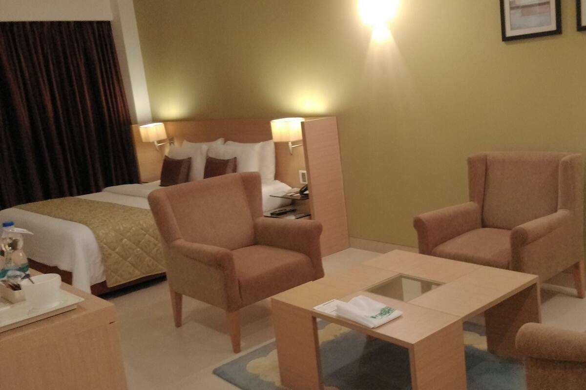 A hotel room with a bed, two armchairs, a small table, a desk, and a mirror.