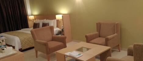 A hotel room with a bed, two armchairs, a small table, a desk, and a mirror.