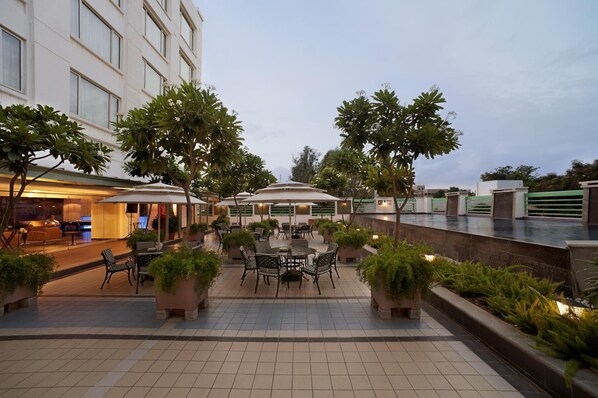 A hotel courtyard with outdoor seating, potted plants, and a pool area. - Radha Regent - Electronics City (Bengaluru)