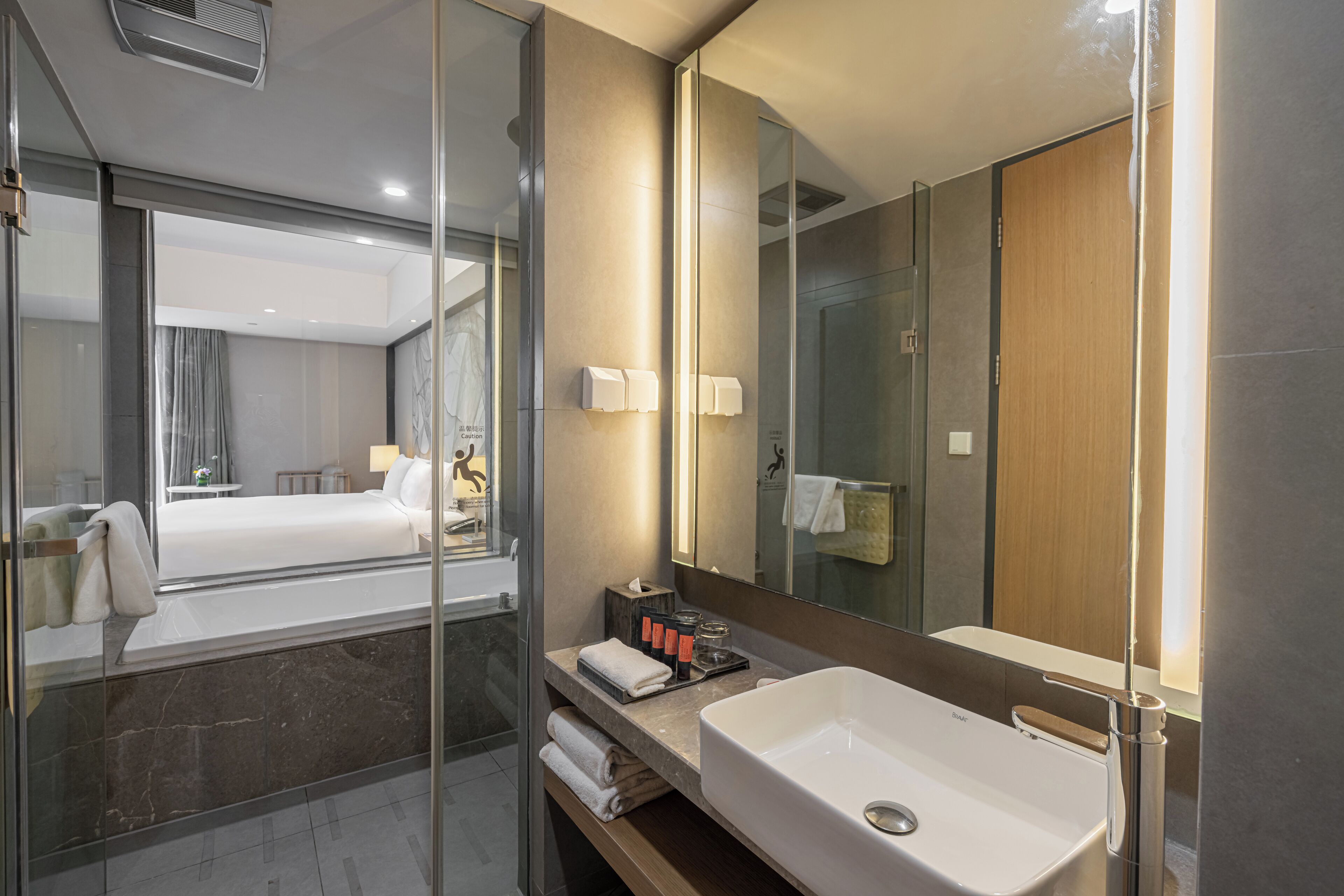 A modern hotel bathroom with a large mirror, a white sink, and a glass-enclosed shower area.