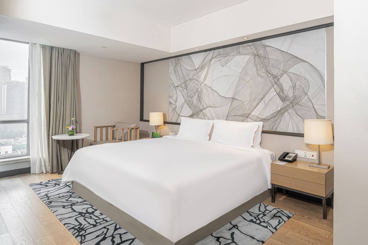 Een moderne hotelkamer met een groot bed, bedlampen, een klein tafeltje en uitzicht op de stad.